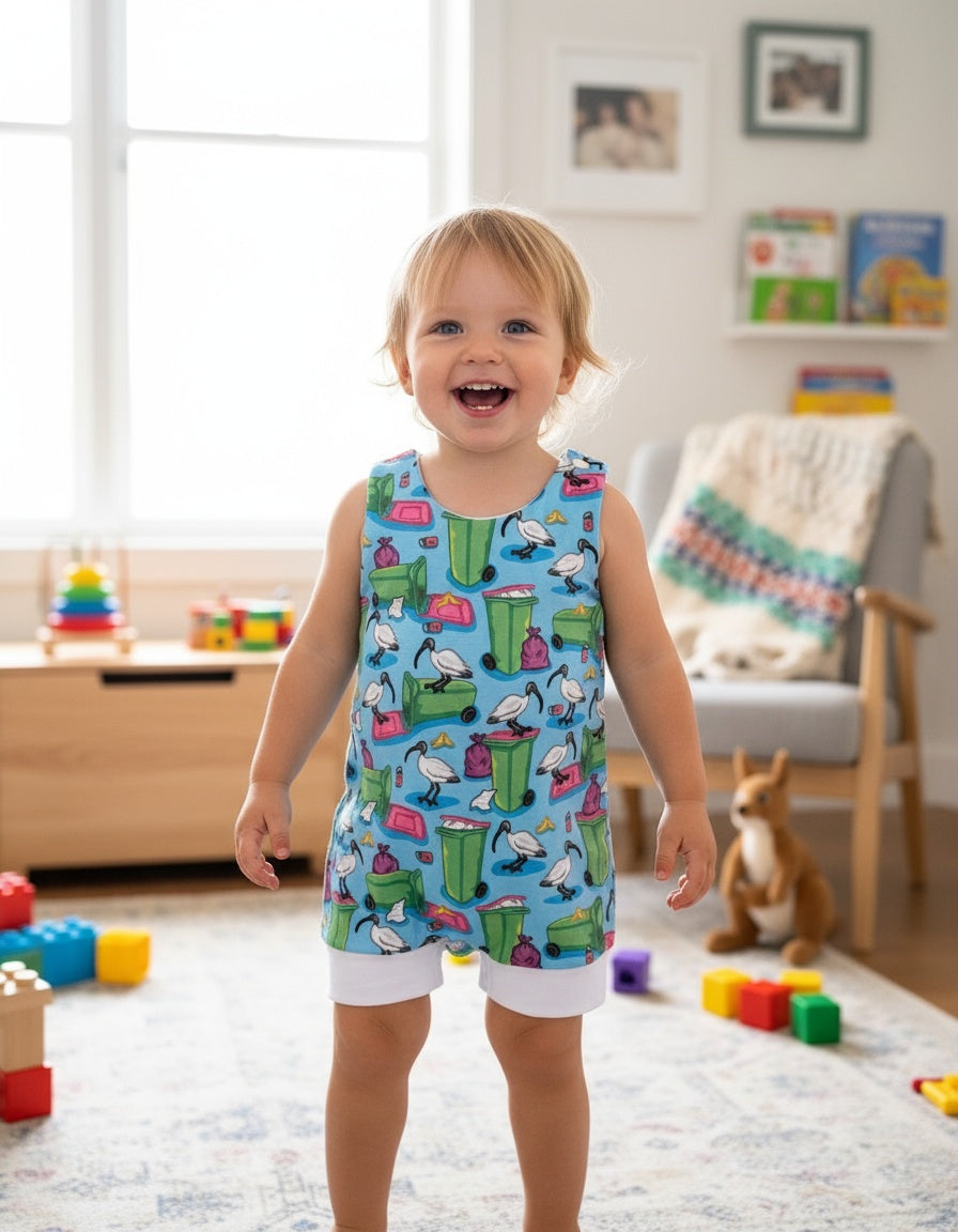 Child wearing a colorful romper with animal patterns in a room with toys and furniture.